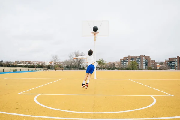 Młody chłopiec gra na żółty boisko do koszykówki zewnątrz. — Zdjęcie stockowe