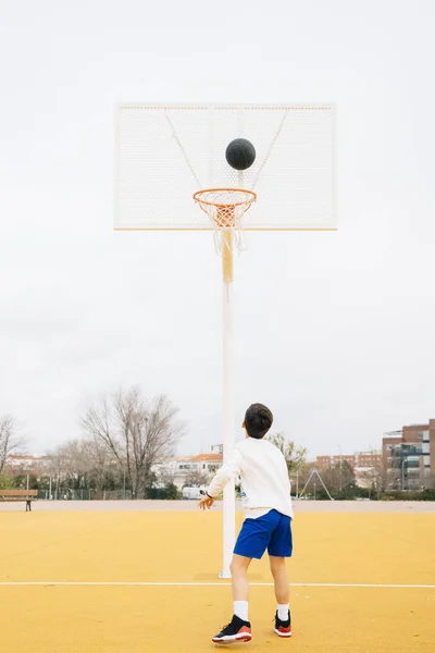 Mladý chlapec hraje na žlutém basketbalovém hřišti venku. — Stock fotografie