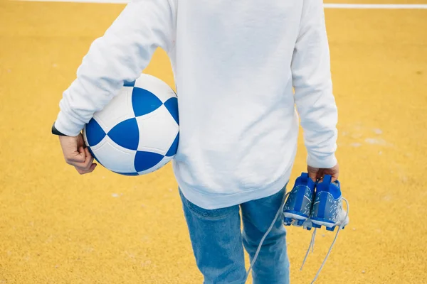 Дитячий футболіст спиною з м'ячем в руці і черевиками в руці — стокове фото