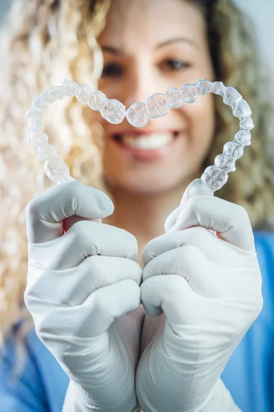 Médico femenino sosteniendo dos alineadores dentales transparentes en forma de corazón —  Fotos de Stock