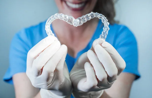 Médico femenino sosteniendo dos alineadores dentales transparentes en forma de corazón —  Fotos de Stock