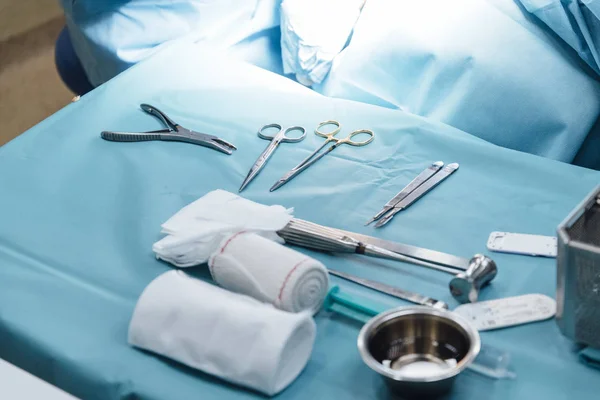 Pohled na sadu lékařských nástrojů umístěných na stole na místě světla v blízkosti nepoznatelného chirurga na operačním sále — Stock fotografie