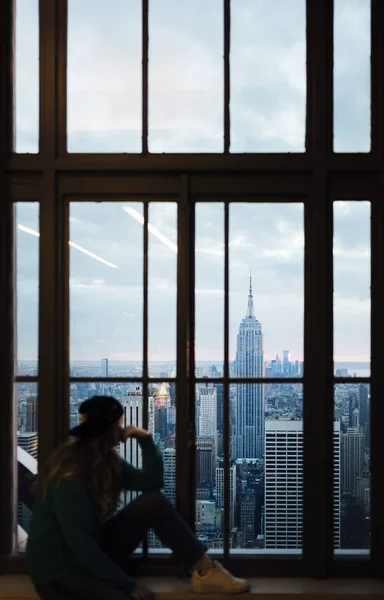 Fotografia de uma mulher olhando para fora da janela de um edifício alto sobre Manhattan. — Fotografia de Stock