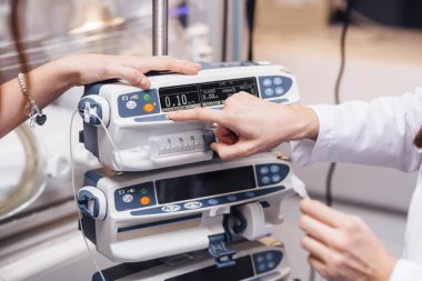 Back view of crop unrecognizable woman in white medical scrub is focusing on screen and adjusting settings of contemporary digital medical equipment in hospital