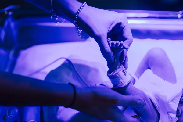 Parent gently touching fragile newborn in neonatal incubator