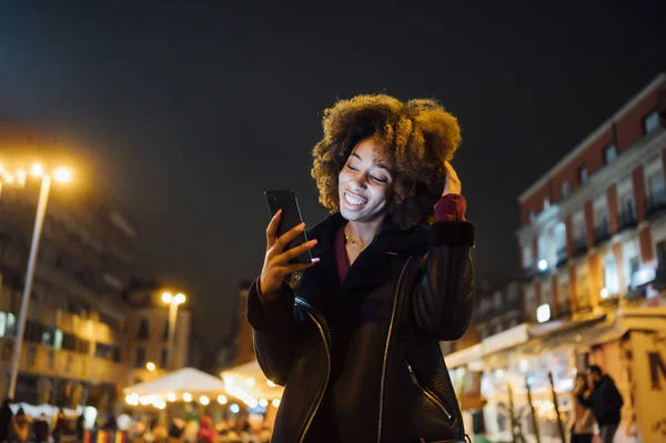 Afro woman with smartphone by the city of Madrid at night — Stock Photo, Image