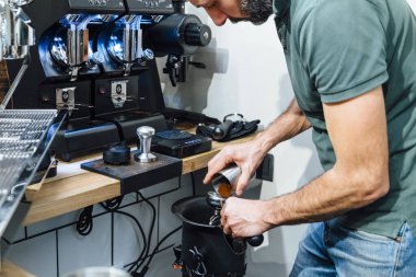 Tanımlanamayan erkek baristanın yakın plan görüntüsü espresso yaparken öğütülmüş kahveyi sıkıştırıyor