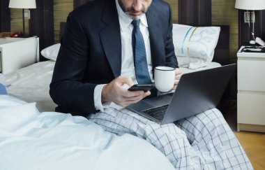 Yataktan yeni çıkmış, bilgisayarlı ve akıllı telefonlu bir iş adamı.