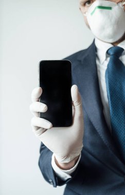 Maskeli ve lateks eldivenli bir iş adamı akıllı telefon kullanıyor.