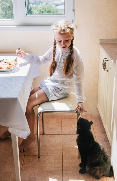 Niña alimentando a un gato negro — Foto de Stock