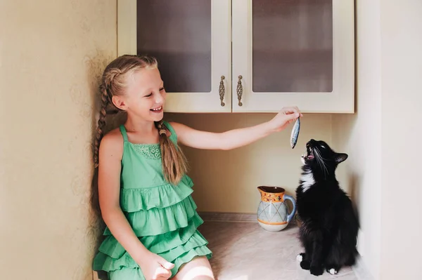 Child girl feeding a black cat