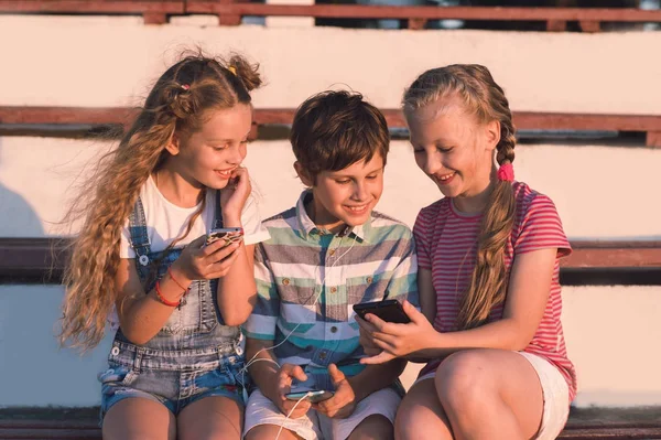 Retrato Tres Niños Preadolescentes Sentados Banco Jugando Teléfonos Inteligentes Escuchando Fotos de stock libres de derechos