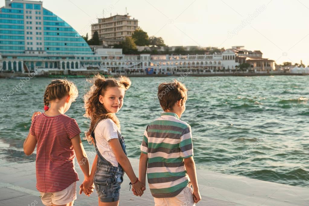 Portrait of three happy preteen children walk along the waterfront