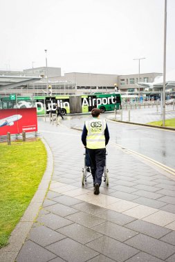 Dublin Havaalanı üye personel yaz yağmurlu günde, Dublin Airport, 14 Ağustos 2017 bina Havalimanı'na tekerlekli sandalye Engelli Yolcu için bastırıyor