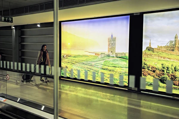 Dublin Airport people, passengers travelling with suitcases on walkway escalator in motion with highlighted images of Ireland in the background, Dublin Airport, Terminal 1, Ireland, 15 August 2017 — Stock Photo, Image