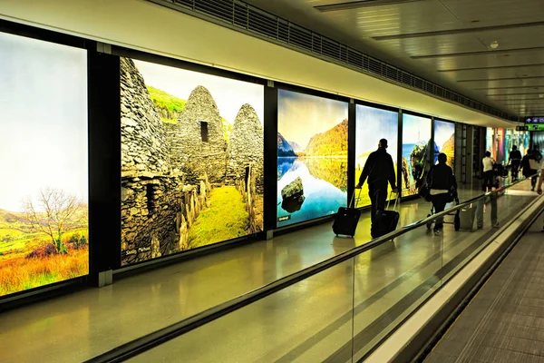 Dublin Airport people, passengers travelling with suitcases on walkway escalator in motion with highlighted images of Ireland in the background, Dublin Airport, Terminal 1, Ireland, 15 August 2017 — Stock Photo, Image