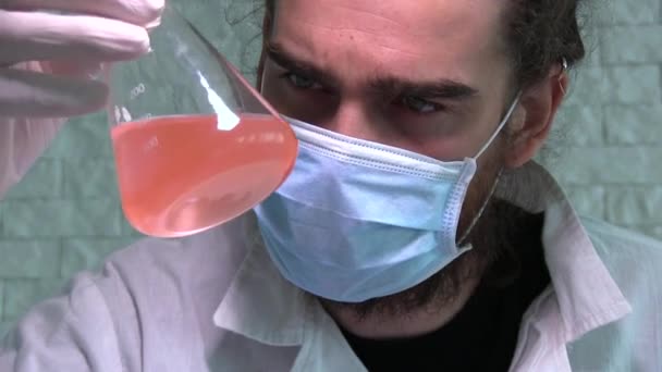 Científico joven está examinando la reacción química en el frasco — Vídeo de stock