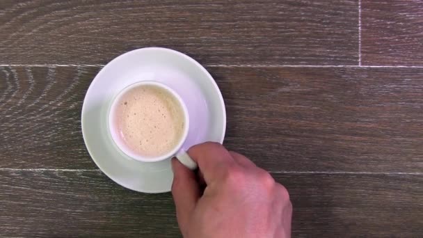 Мужчины рука берет белую чашку с кофе стоит на коричневом столе — стоковое видео