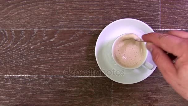 Mann steckt den Zucker in eine weiße Tasse mit Kaffee auf einem braunen Tisch — Stockvideo