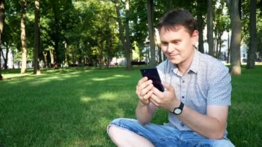 Şehir Parkı yeşil çim adam Smartphone ile oturur