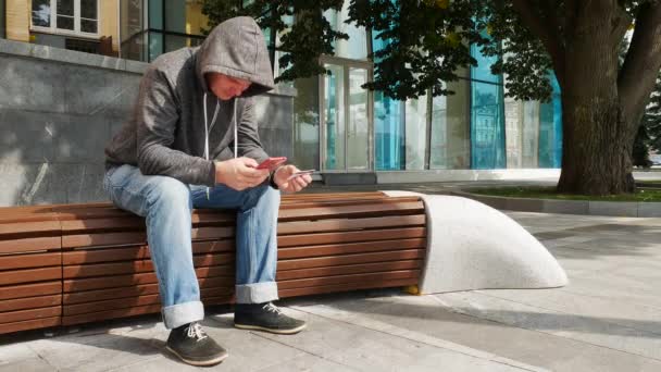 Homem com capuz segurando smartphone vermelho e cartão de crédito ou débito — Vídeo de Stock