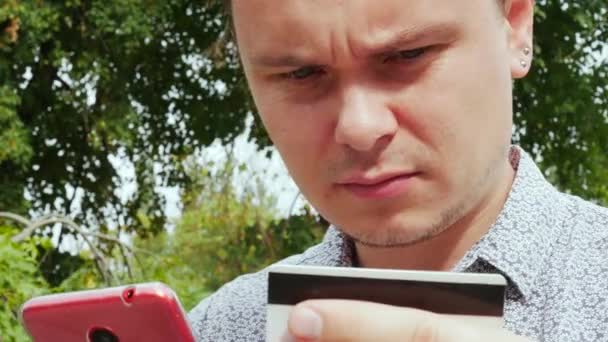 Homem segurando smartphone vermelho e cartão de débito ou crédito — Vídeo de Stock