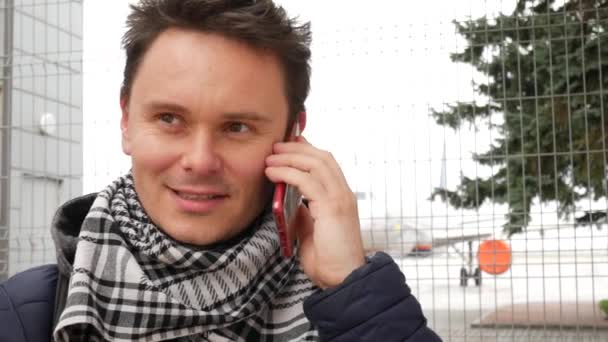 Genç gülümseyen ve Havaalanı'nda kırmızı akıllı telefonda konuşan adam — Stok video
