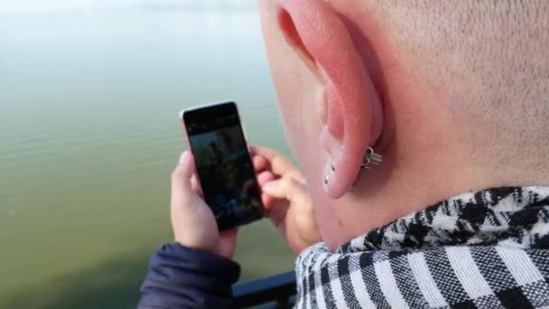 Holohlavý muž s třemi náušnice v uchu používá chytrý telefon — Stock video