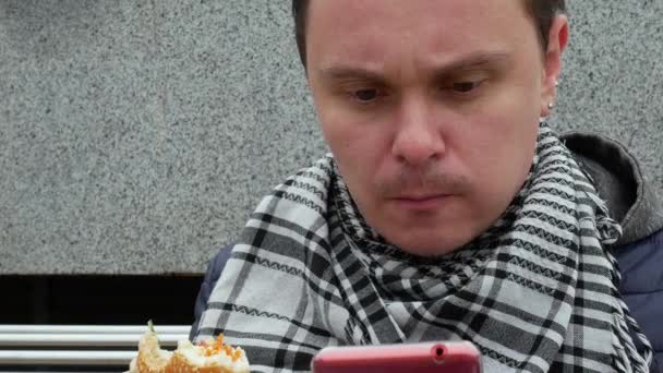 Ο άνθρωπος τρώει σάντουιτς και χρησιμοποιώντας έξυπνο τηλέφωνο — Αρχείο Βίντεο