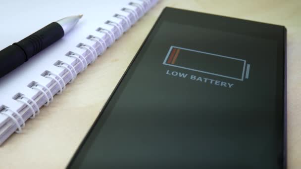 Bateria fraca no smartphone na mesa do escritório com caneta e bloco de notas — Vídeo de Stock