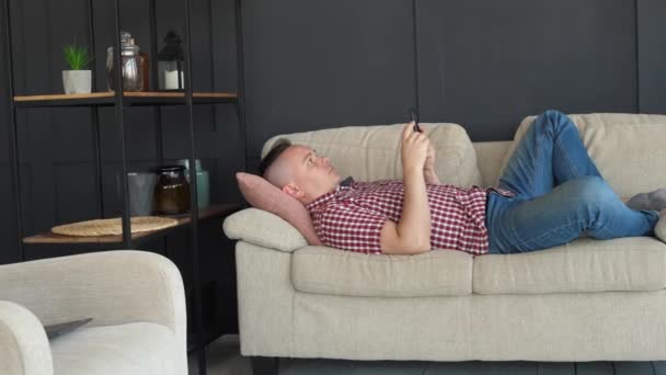 Una persona se encuentra en el sofá y el uso de Smartphone — Vídeos de Stock
