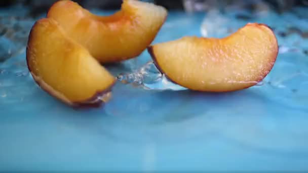 Wasser fällt und plätschert auf Pflaumenscheiben vor blauem Hintergrund — Stockvideo