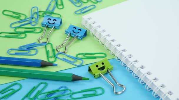 Zöld és kék irodai papír klip, mosoly kötőanyag klipek és ceruzák jegyzettömbön — Stock videók