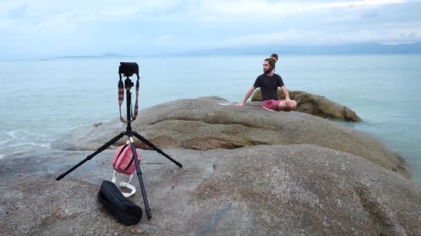 Man Vlogger Yogi skjuter video för sociala nätverk webbplats på klippan nära havet — Stockvideo