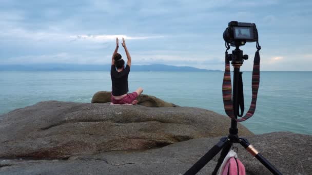 Männlicher Yogalehrer zeichnet Video von Praxis auf Felsen am Meeresufer für Social-Media-Seite auf — Stockvideo