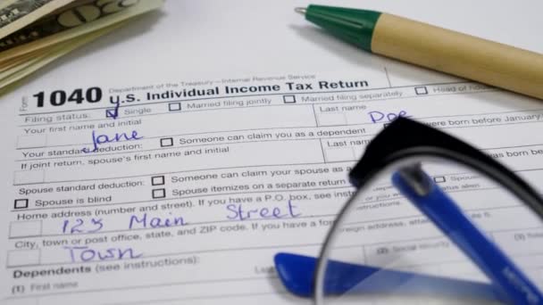 Notas de dólar, caneta e óculos no formulário de declaração de imposto 1040 — Vídeo de Stock