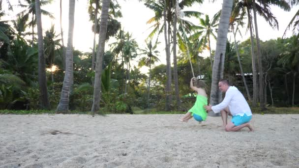 Vater rollt Tochter auf Seil am Strand auf Palme — Stockvideo