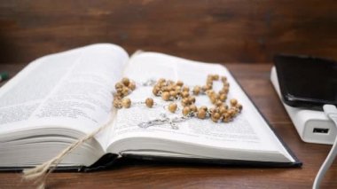 Kutsal İncil 'i boncuklarla aç ve kahverengi ahşap masada çarmıha geril.