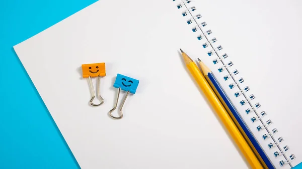 Orange Color and Blue Smile Binder Clips with Yellow Blue Pencils on Paper Notepad