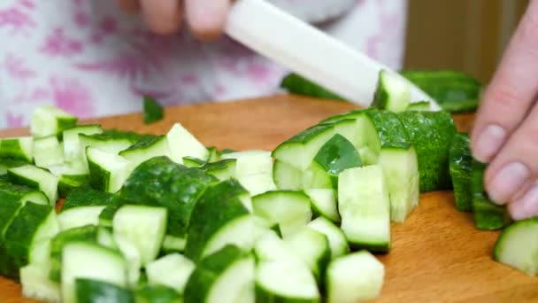 Vrouwen handen gesneden groene komkommer in stukken op snijplank door mes — Stockvideo