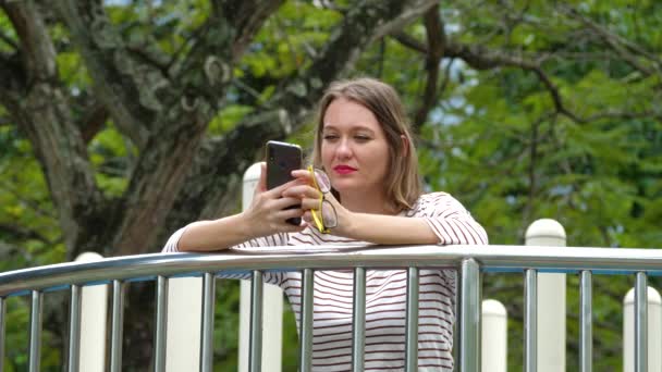 Милая женщина с помощью смартфона на зеленом фоне дерева — стоковое видео