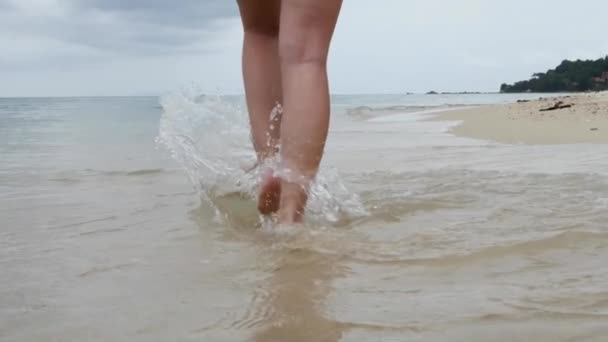 Piernas femeninas en la orilla arenosa con olas de agua salpicando — Vídeo de stock