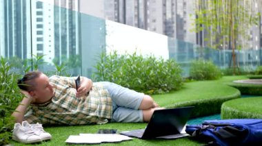 Relaxed male using smartphone and Tablet PC on green grass