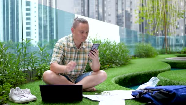 Мужчина работает с бумажными документами с использованием черного смартфона и ноутбука — стоковое видео