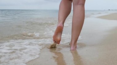 Female legs on sandy beach with splashing water wave