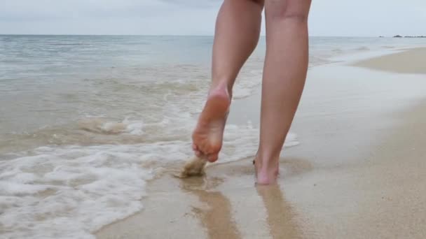 Женские ноги на песчаном пляже с брызгающей волной воды — стоковое видео