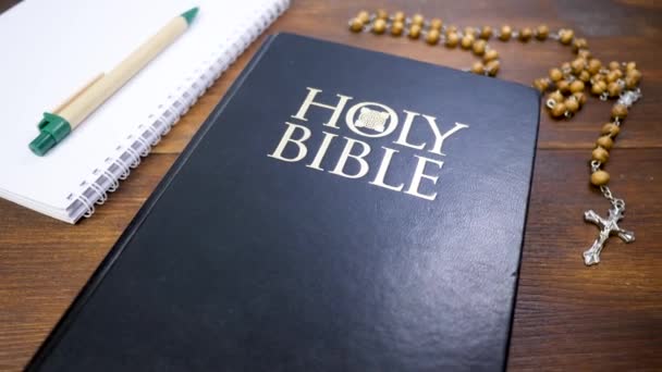 Священна Біблія з бісером з розп'яттям на коричневому дерев'яному столі фоні — стокове відео