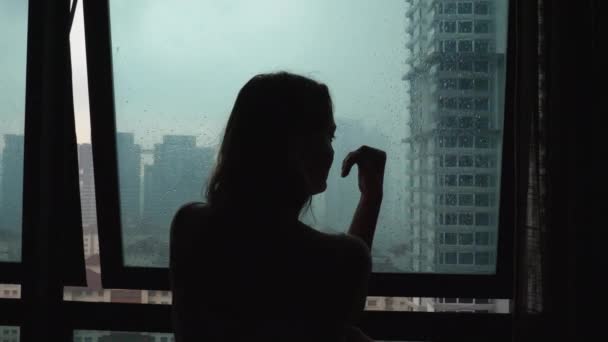 Силует сумна самотність жінка торкається скляного вікна в день дощу — стокове відео