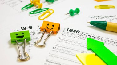 Smile Orange and Green Binder Clips with Pen on 1040 Tax Form and W-9