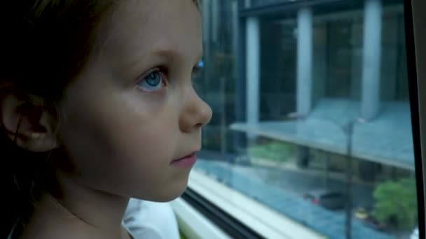 Little child girl looks out window of train in carriage during journey — Stock Video